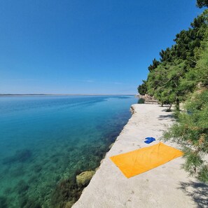 A coastal view with clear water, a sandy beach, and a rocky outcrop with trees.