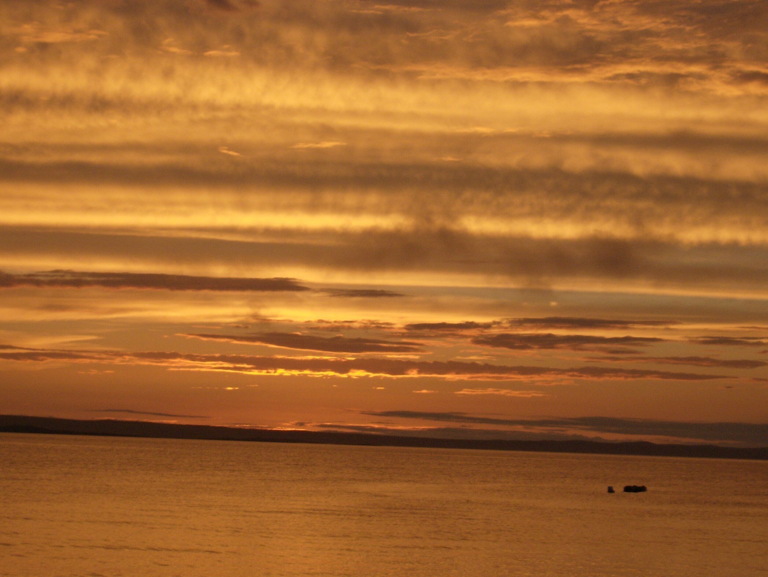 A sunset over a body of water with a distant boat.