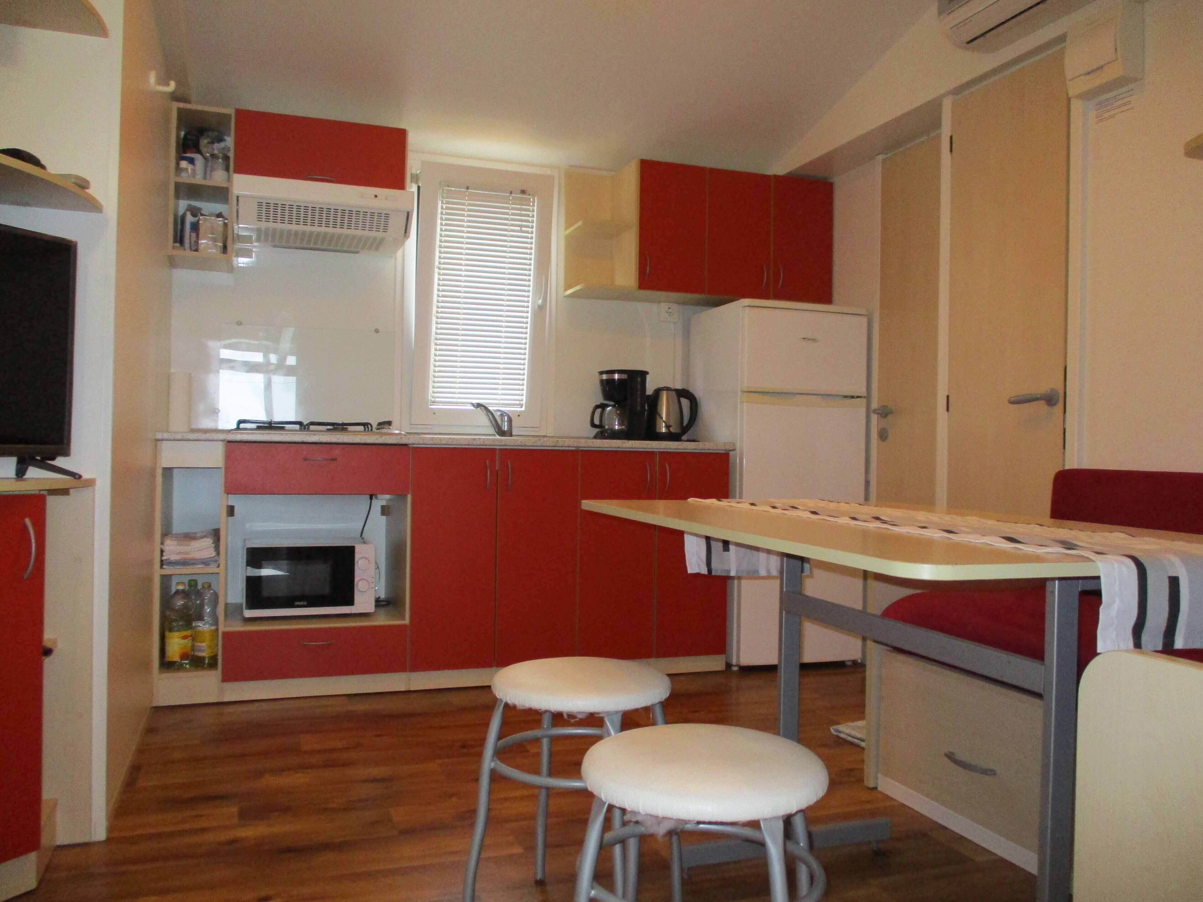 A compact kitchen with a microwave, stove, and refrigerator. There are two stools and a small table.