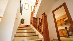Eine Treppe mit Holzbalkonen und beigefarbenen Stufen führt zu einem Küchenbereich mit Holzausbau und Fliesenboden.