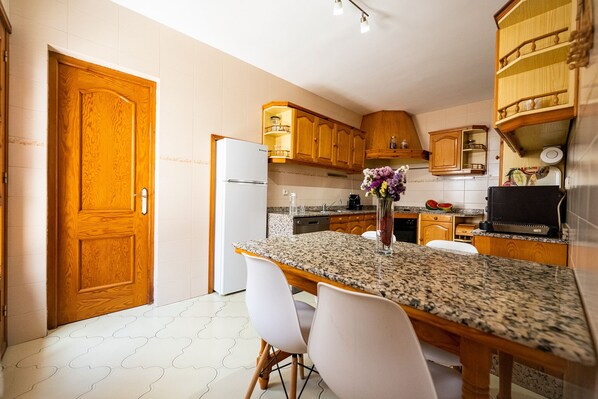 Una cocina con armarios de madera, encimera de granito y sillas blancas.
