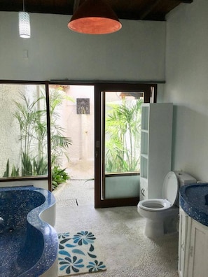 Un baño con bañera, inodoro y lavabo. Se ve vegetación a través de la ventana.