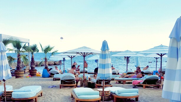 A beach with lounge chairs and umbrellas, a building with a balcony, and the ocean in the background. - Charming 1 Bedroom Apartment for 2 Guests (Sunny Beach)