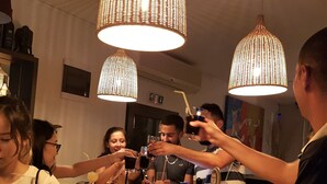 A bar area with hanging pendant lights, a bar counter, and a group of people toasting with drinks. - Charming 1 Bedroom Apartment for 2 Guests (Sunny Beach)