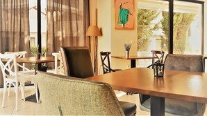A dining area with a wooden table, chairs, and a lamp. There is a painting on the wall and a window with curtains. - Charming 1 Bedroom Apartment for 2 Guests (Sunny Beach)