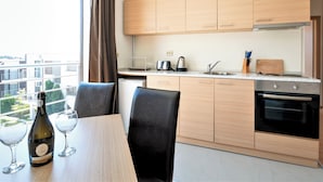 A modern kitchen with wooden cabinets, a built-in oven, and a dining area with a table and chairs. - Seaside 1 BR Apartment With Balcony, up to 4 Pax (Sunny Beach)