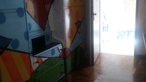 Quarto com design abstrato e colorido na parede, piso de madeira e porta que dá para área externa.