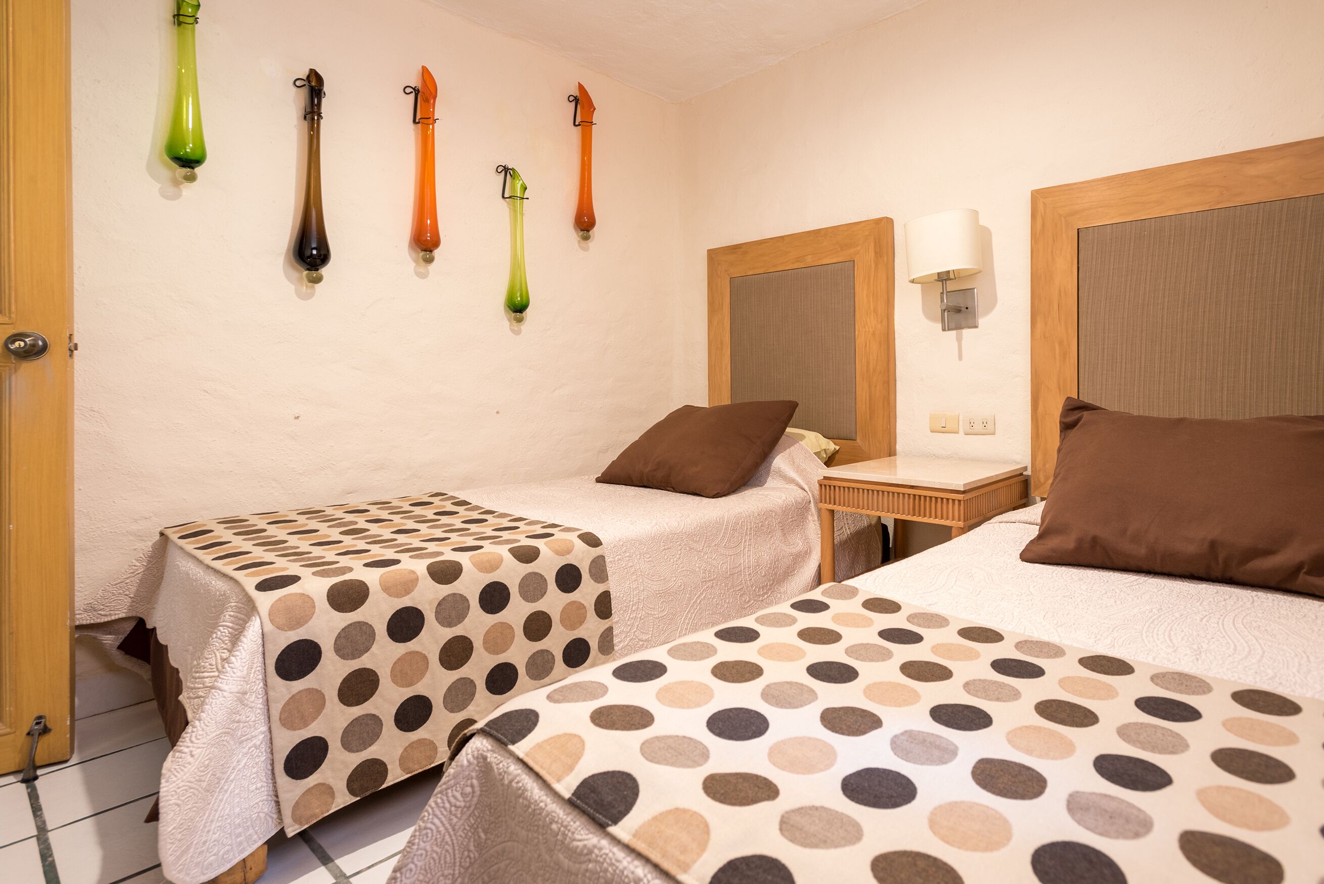 Habitación de hotel con dos camas, una mesita, una lámpara de pared y una mesita de noche.