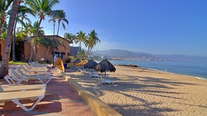 A beachside hotel with lounge chairs, palm trees, and a view of the ocean. - Villa Facing the Beach in a Large Terrace 7 Pools, Tennis Courts, 247 Security (Puerto Vallarta)