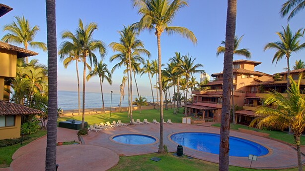 A resort with a pool area, palm trees, and a view of the ocean. - Villa Facing the Beach in a Large Terrace 7 Pools, Tennis Courts, 247 Security (Puerto Vallarta)