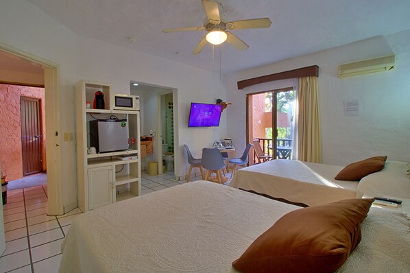 A hotel room with two beds, a television, a desk with a chair, and a balcony.
