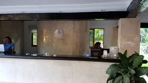 A reception desk with a sign reading "RECEPTION FRONT DESK," a logo on the wall, and a potted plant to the right. - Villa Facing the Beach in a Large Terrace 7 Pools, Tennis Courts, 247 Security (Puerto Vallarta)