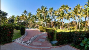 A paved pathway leading to a pool area surrounded by palm trees and lush greenery. - Villa Facing the Beach in a Large Terrace 7 Pools, Tennis Courts, 247 Security (Puerto Vallarta)