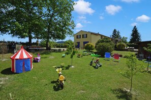 A grassy yard with a small tent, a yellow bicycle, and a blue and red playhouse. - Casa Sofi (Monticiano)
