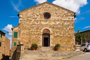 A stone building with a central arched doorway, steps leading up to it, and two potted plants on either side. - Casa Sofi (Monticiano)