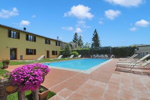 A swimming pool with lounge chairs, a yellow building, and a clear blue sky. - Casa Sofi (Monticiano)