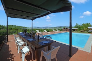 A covered outdoor dining area with a pool, chairs, and a table set for dining. - Casa Sofi (Monticiano)