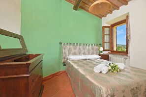 A bedroom with a bed, a wooden dresser, a window with a view, and a lamp. - Casa Sofi (Monticiano)