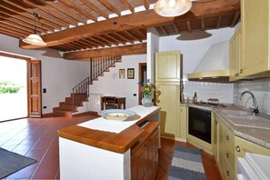 A kitchen with wooden beams, a dining area with a table and chairs, and a staircase leading to another level. - Casa Sofi (Monticiano)