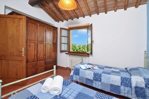 Un dormitorio con un armario de madera, una ventana con vistas, dos camas con ropa de cama azul y un ventilador de techo.