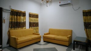 Ein Wohnzimmer mit zwei gelben Sofas, gemusterten Vorhängen, einer Chandelierleuchtre und einer Klimaanlage.