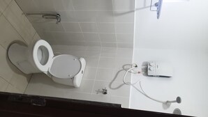 Des toilettes blanches dotées d’un siège-bidet, d’un sèche-mains et d’un robinet mural, dans une salle de bain dont le sol est recouvert de carreaux blancs.