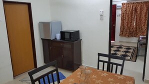 A small room with a wooden door, a cabinet, a microwave, a table with a patterned tablecloth, and a chair.