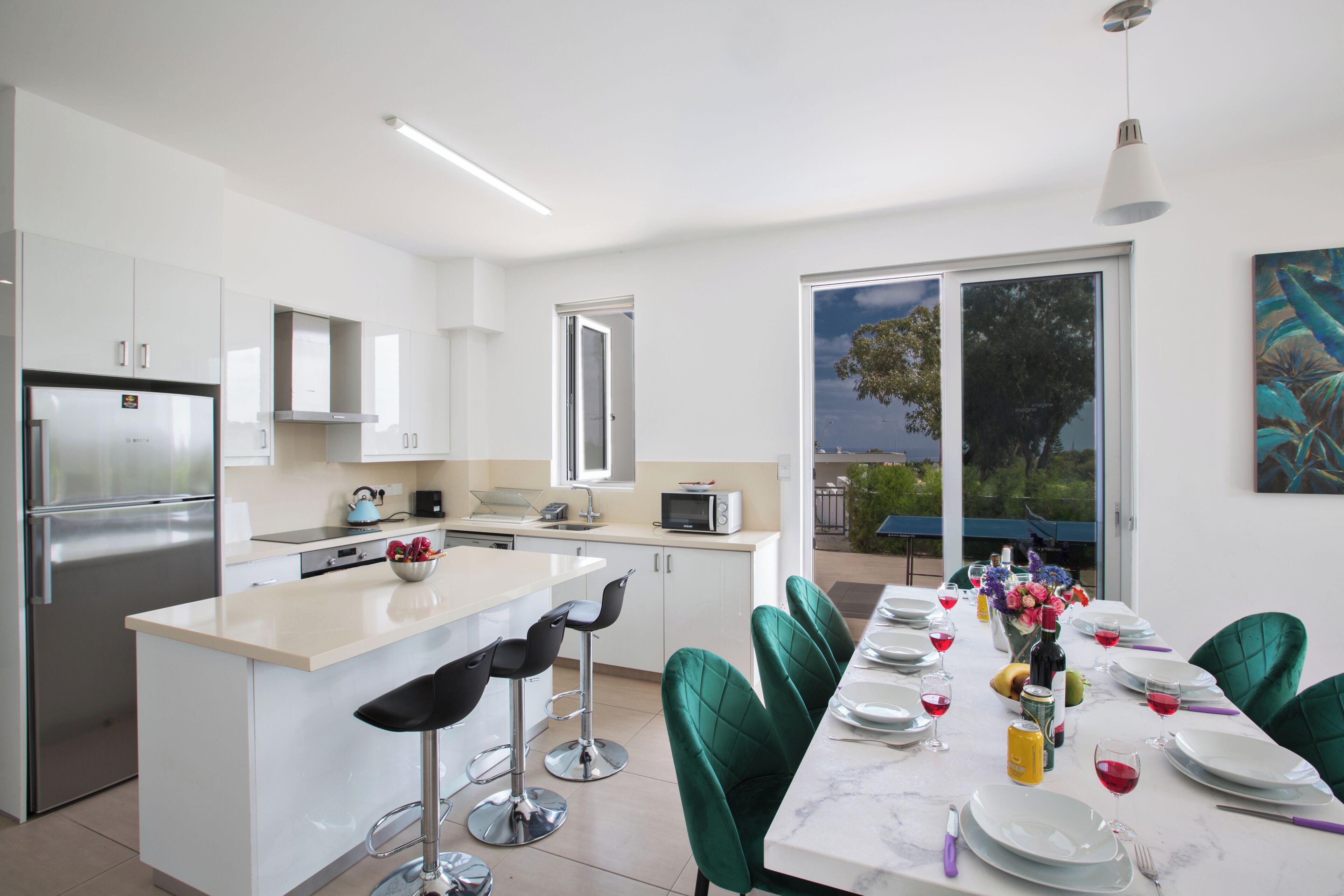 Una cocina moderna con una isla central, taburetes de bar y un comedor con mesa para cuatro.