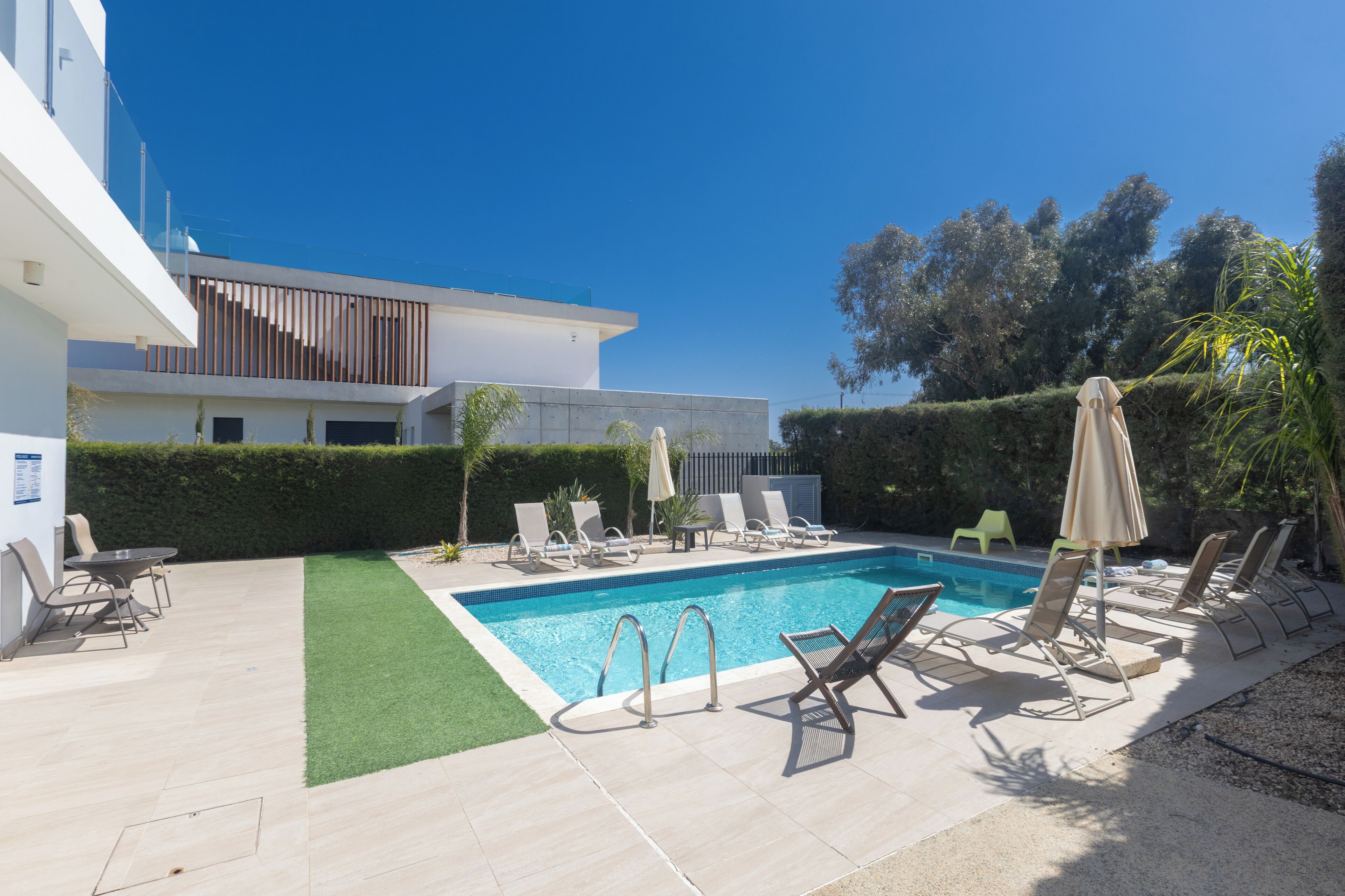 A modern pool area with lounge chairs, a pool, and a building with a flat roof and large windows.