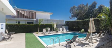 A modern pool area with lounge chairs, a pool, and a building with a flat roof and large windows.