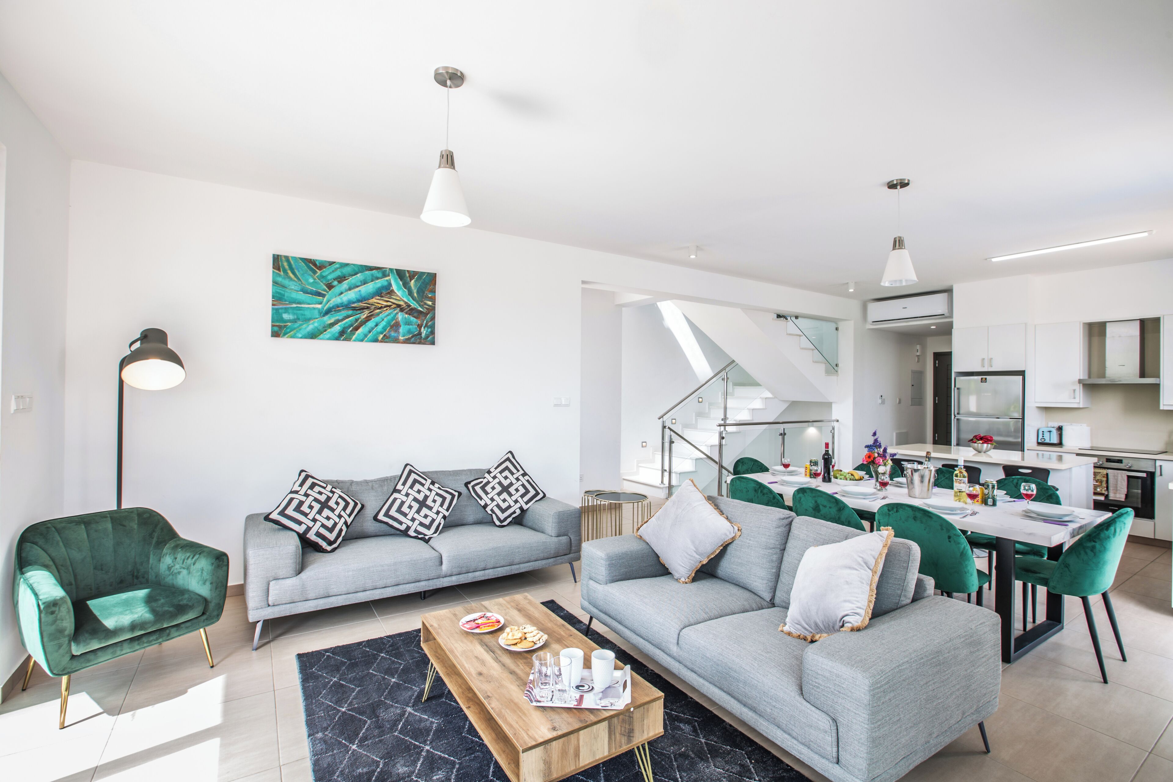 Ein modernes Wohnzimmer mit grauem Sofa, grünem Sessel und einem Essbereich mit Tisch und Stühlen.