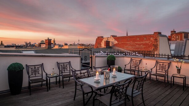 A rooftop terrace with a table set for two, surrounded by chairs, and a view of the city skyline at sunset. - Comfy Apartment in Berlin (Berlin)