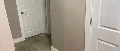 Un pasillo con suelo de madera, paredes blancas y una puerta blanca al final.