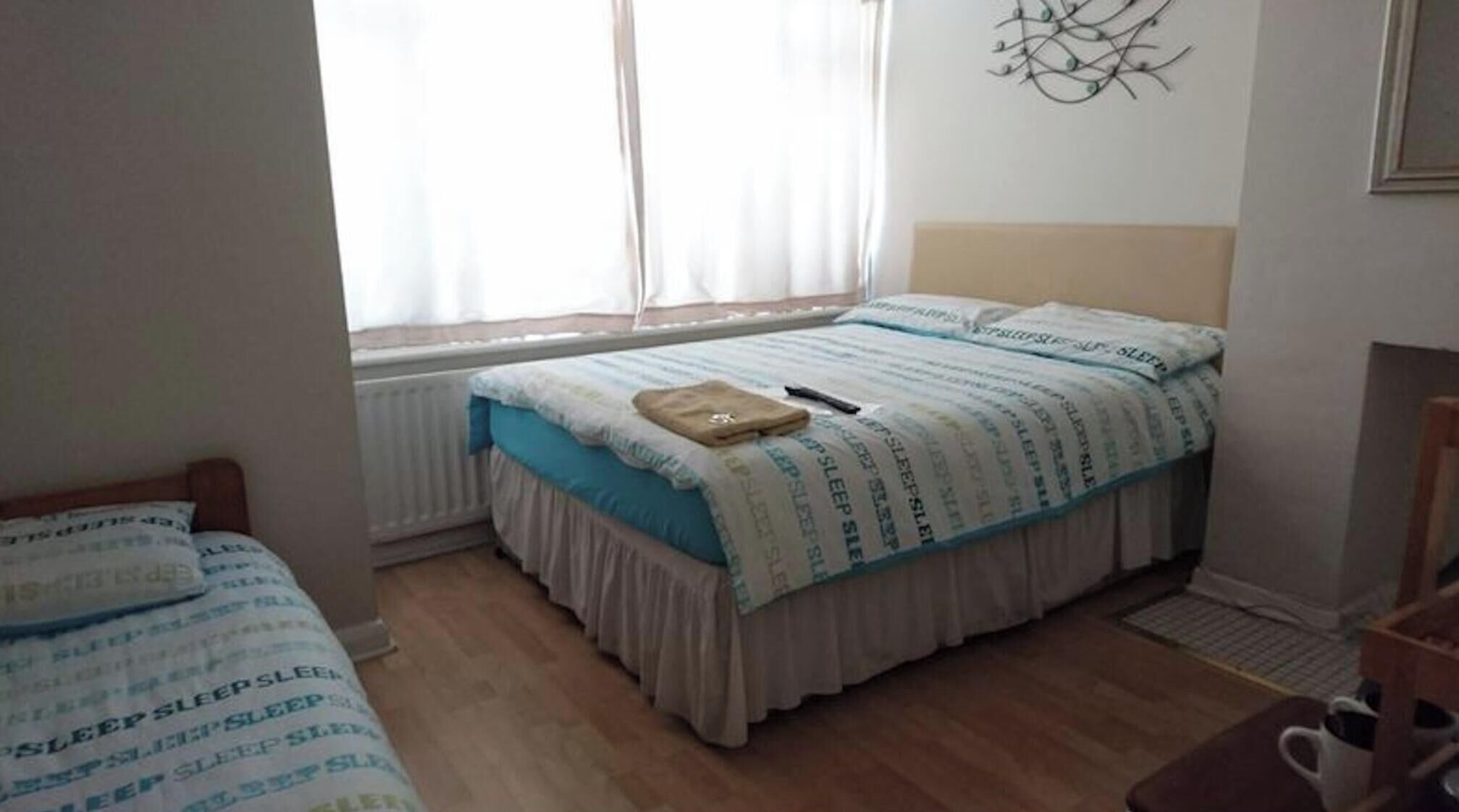 Une chambre à coucher avec un lit, une table de chevet, une fenêtre avec des rideaux et un radiateur.