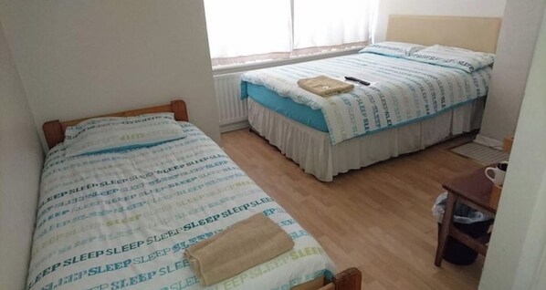 A small, single-bed room with a wooden headboard, a window with curtains, and a radiator. - Room-family Room Sleeps 3 With 1 Double (Hayes)