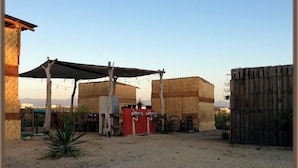 Un espacio al aire libre rústico con una estructura de madera, una mesa de metal y un armario rojo.