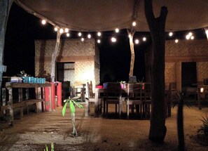 Een buitenruimte met een eethoek, versierd met lichtslingers, houten tafels en stoelen.