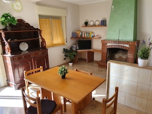 Ein gemütliches Wohnzimmer mit einem Holzesstisch, Stühlen, einem Kamin, einem Fernseher und einem Bücherregal.