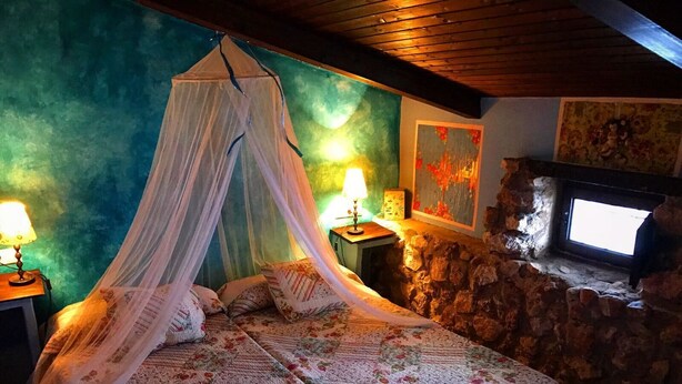 A bedroom with a canopy bed, stone wall, and a fireplace.