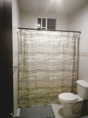 A bathroom with a striped shower curtain, a toilet, and a small window above the shower.