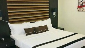 Une chambre d’hôtel avec un lit, une table de chevet, une lampe fixée au mur et un tableau.