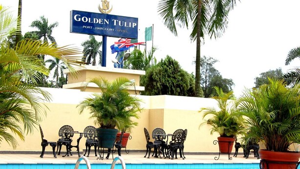 A pool area with lounge chairs and potted plants, a sign for Golden Tulip Port-Harcourt Hotel, and palm trees. - Room-golden Tulip Port Harcourt-guest Ro (Port Harcourt)