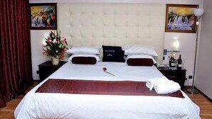 A hotel room with a large bed, a nightstand with a lamp, a vase with flowers, and artwork on the walls. - Room-golden Tulip Port Harcourt-guest Ro (Port Harcourt)