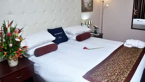 A hotel room with a tufted headboard, a bed with white and red bedding, a bedside table with a lamp, and a floral arrangement. - Room-golden Tulip Port Harcourt-guest Ro (Port Harcourt)