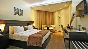 Ein Hotelzimmer mit Bett, Nachttischlampen, einem Schreibtisch mit Stuhl, einem Fernseher und einem großen Fenster mit Vorhängen.