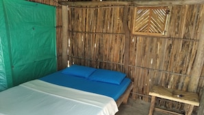 Una cama individual con una colcha blanca y azul, una cortina verde y una pared de madera con un ventanal.
