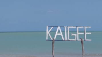 Segnaletica da spiaggia con la scritta "KAIGE" su una spiaggia sabbiosa e acque blu cristalline.