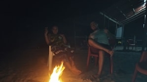 Dos personas sentadas junto a una fogata por la noche.