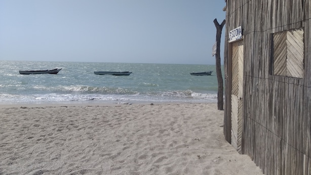 Una playa con tres barcos en el agua y un edificio de madera con un letrero.