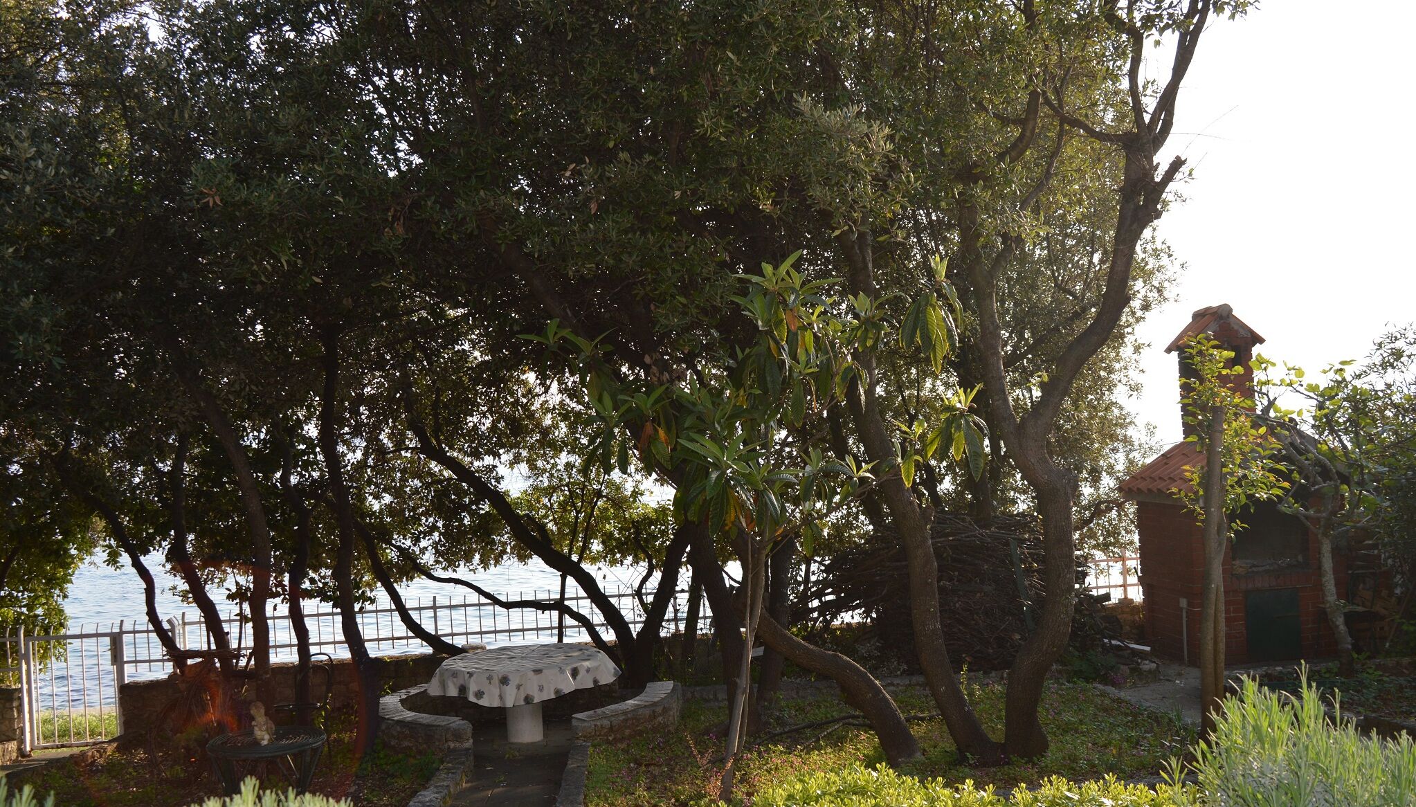 A park with a table and chairs, a fence, and a building with a red roof.
